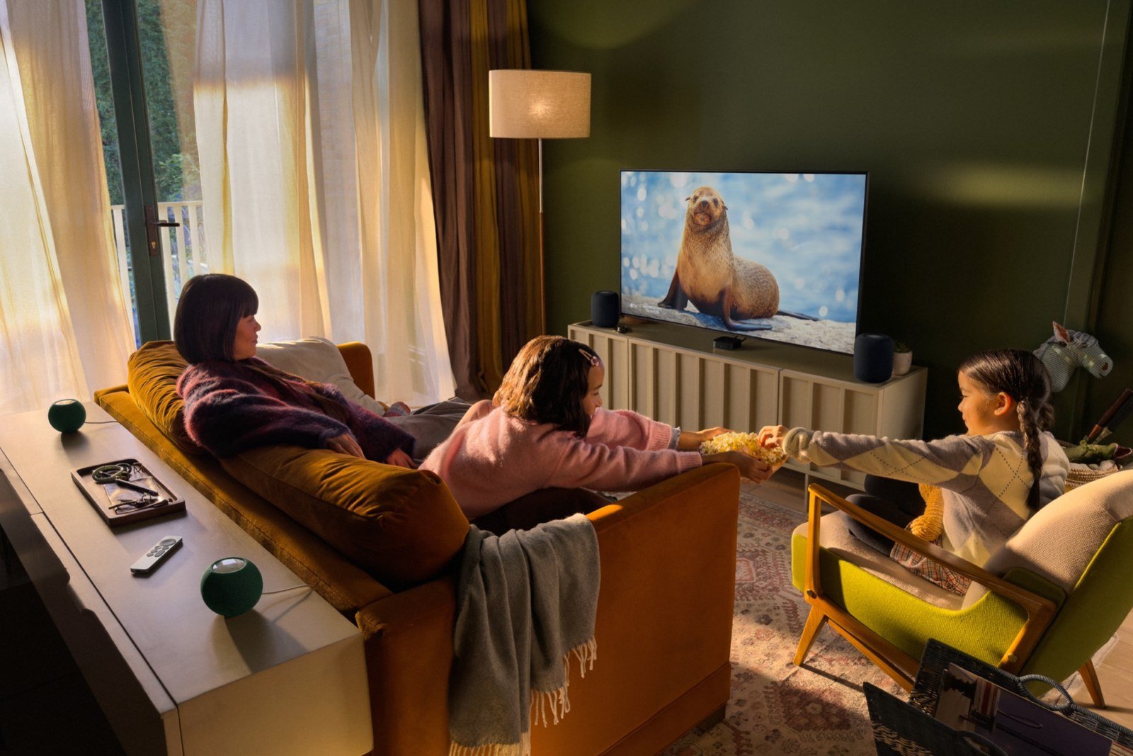 A family watching a nature show on a TV powered by the Apple TV 4K, with HomePod mini 2 speakers set up around the room for surround sound