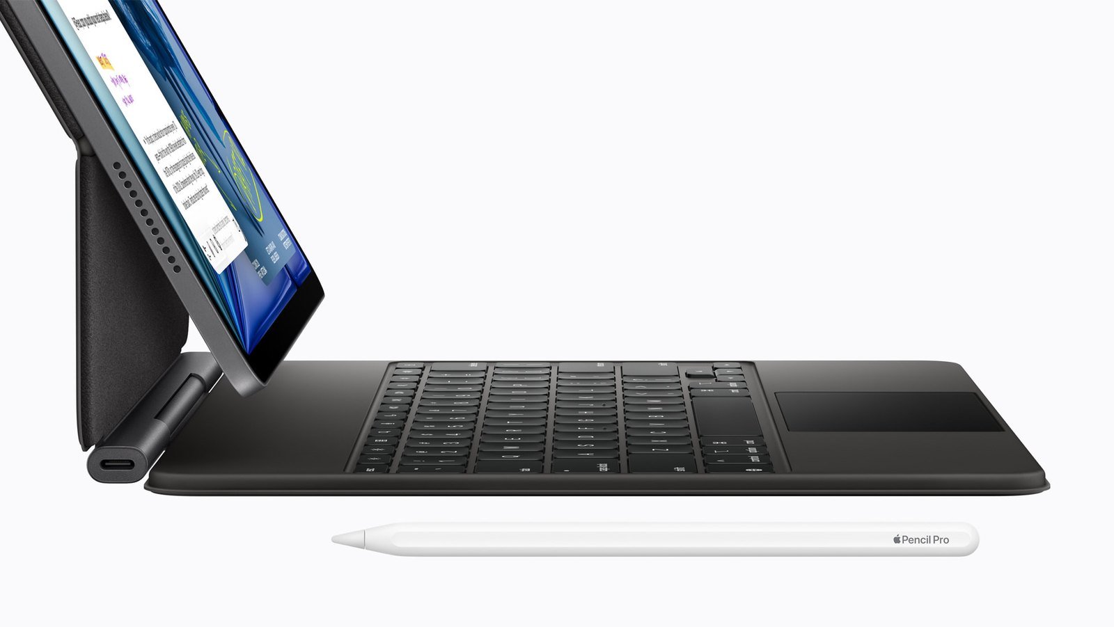 An Apple iPad Air docked in a black Magic Keyboard with an Apple Pencil Pro lying in front of it