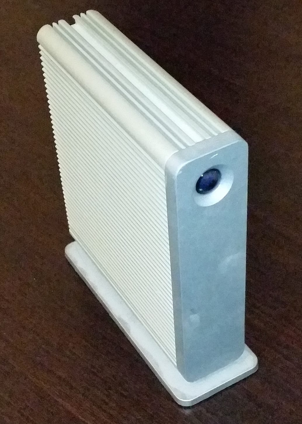 A silver aluminum external desktop hard drive standing upright on a dark wooden desk