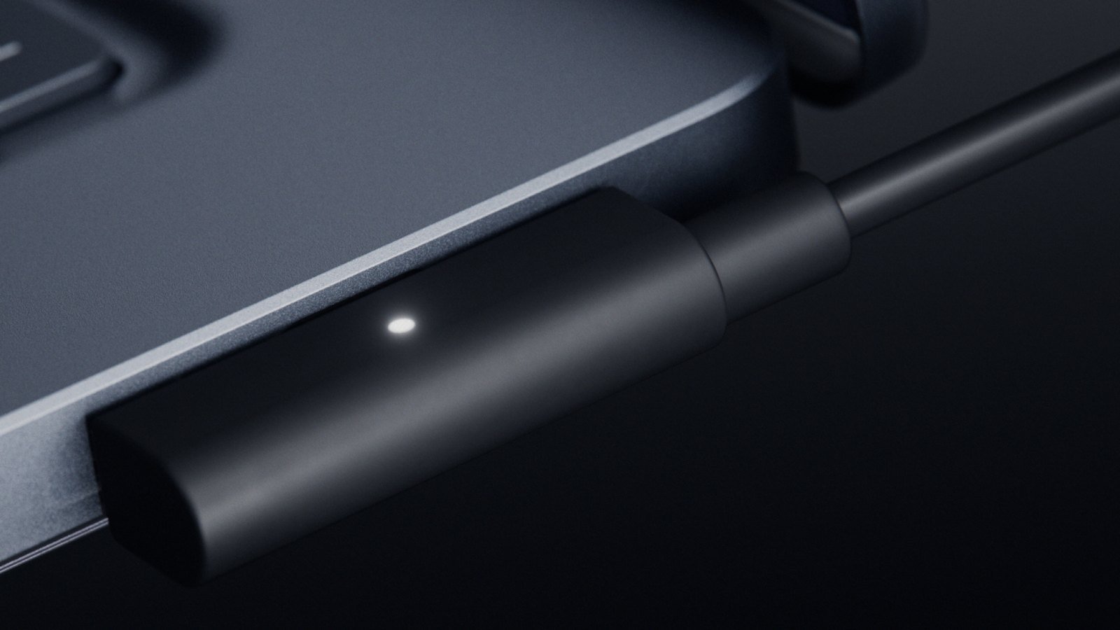 Close-up of a black magnetic USB-C cable clicking into the side of a Surface Laptop Ultra, with a small white status light