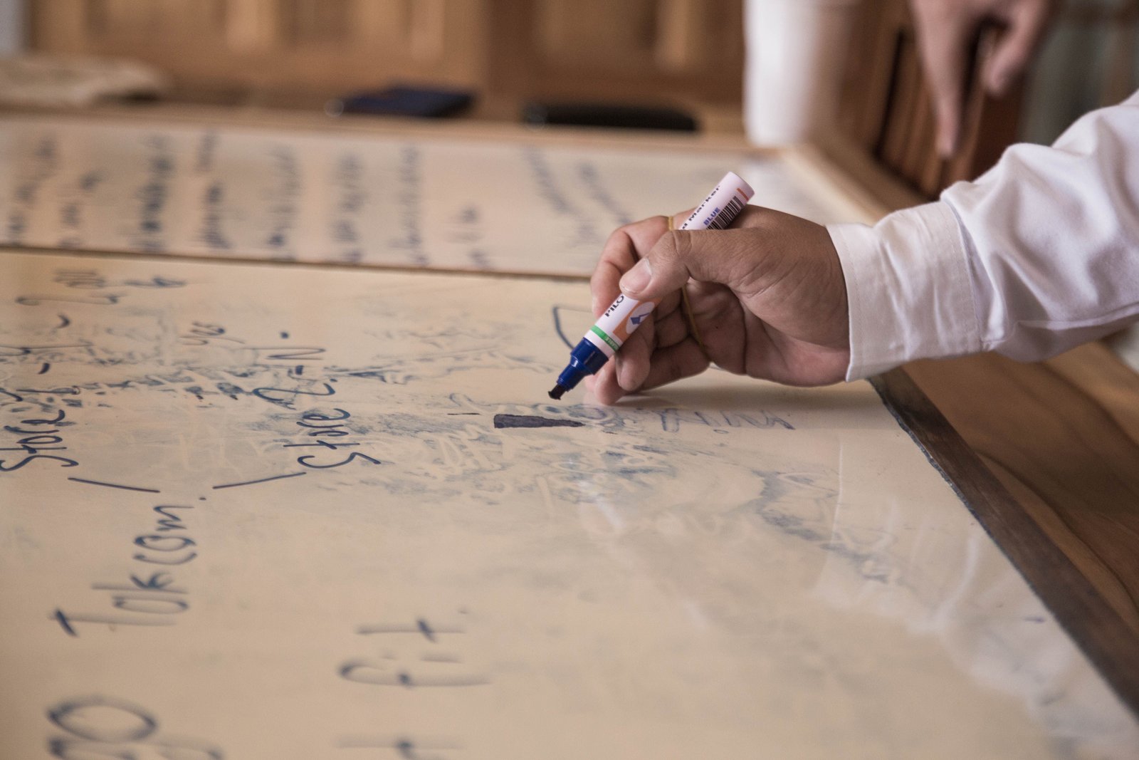 A hand writing on a whiteboard with a marker, office setting