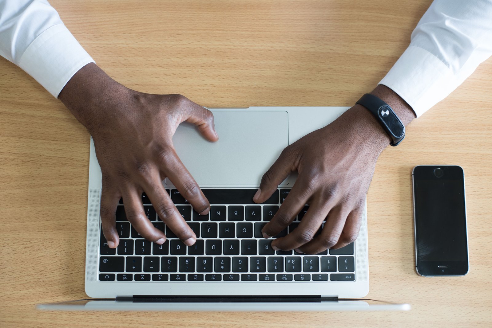 Close-up of hands typing on a laptop keyboard, a smartphone on the desk beside it